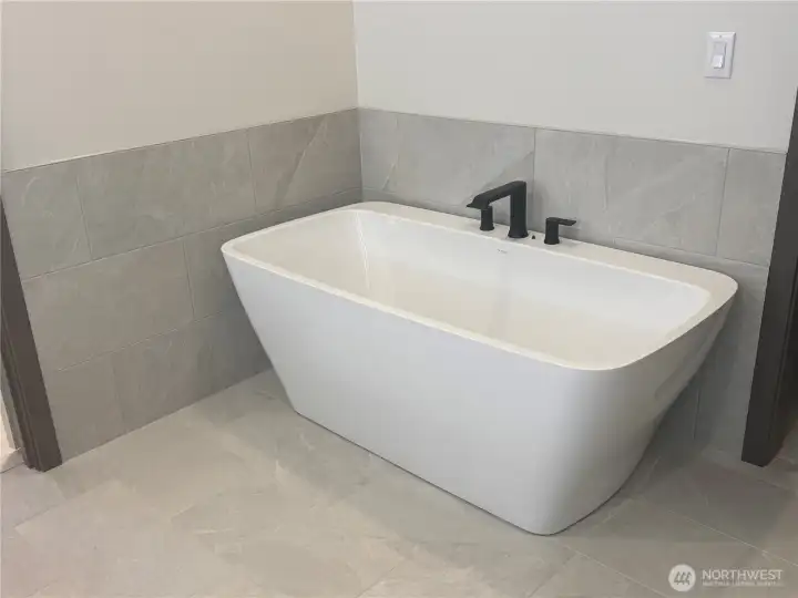Primary bath has a deep free standing tub surrounded by a tile wainscot wall.