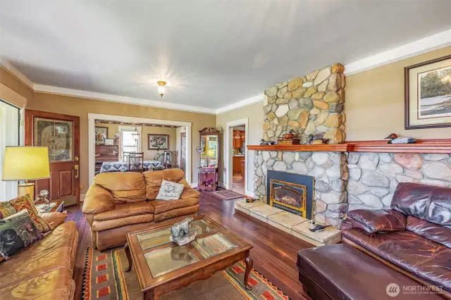 This living room features a beautiful river rock fireplace with a gas insert, creating a cozy ambiance. Large windows frame the breathtaking views, bringing the outdoors in. The space opens seamlessly into the dining room, making it perfect for entertaining and enjoying the scenery.