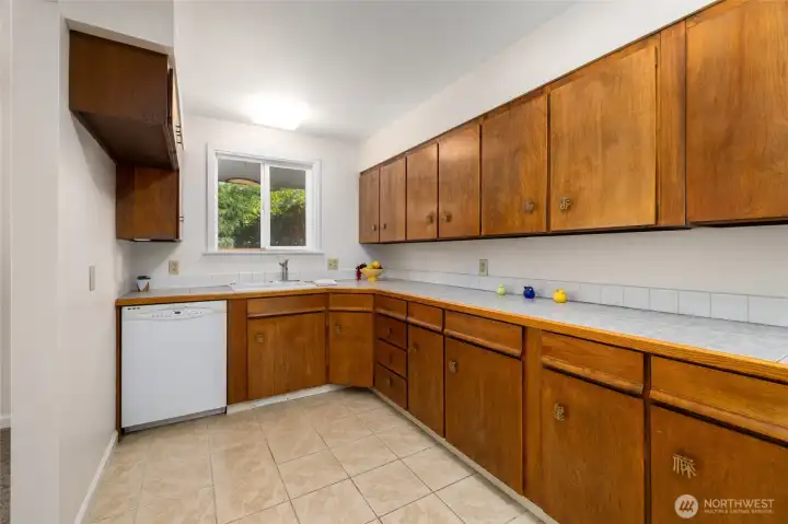 Just off the great room is the kitchen with tile floors and countertops, and wood cabinets.
