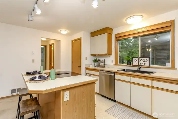 Kitchen with breakfast bar and stovetop. Pantry at the end of the counter.Hallway leads to half bath on right opposite garage door and laundry room at the end of the hall.