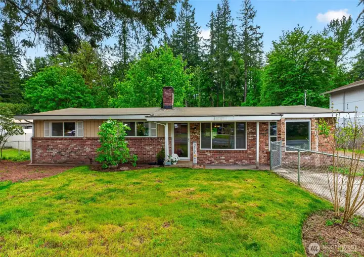 Classic single-level brick rambler with a welcoming front lawn and mature landscaping. Tucked against a backdrop of towering evergreens, this home offers a peaceful neighborhood feel with plenty of outdoor space and timeless character. The covered entry and expansive frontage create a warm first impression with room for personalization