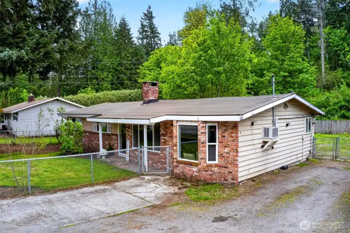 Corner lot positioning and extended driveway provide plenty of space for parking, guests, or recreational vehicles. This classic brick rambler is framed by lush greenery and towering trees, offering a quiet, tucked-away feel while still being close to everyday conveniences. The fenced front yard and covered entry add both charm and functionality to the home’s inviting exterior.