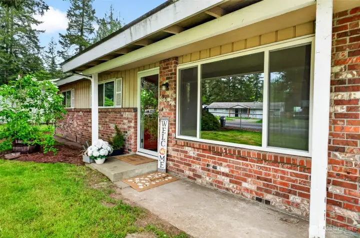 Inviting covered front porch with classic brick detailing and large picture windows that bring in great natural light. The welcoming entry creates a warm first impression, while the mature landscaping and covered walkway add charm and functionality to this well-positioned rambler.