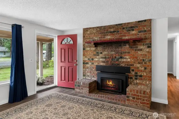 Statement brick fireplace creates a warm focal point in the living area, adding timeless character and a cozy atmosphere to the home. The bright entryway, updated flooring, and open layout make the space feel welcoming and functional, while the large windows bring in natural light throughout the day. A blend of classic charm and comfortable living space gives this room a unique personality.