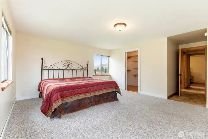 Spacious bedroom with large windows on two sides, bringing in abundant natural light and showcasing surrounding views. Features a walk-in closet and neutral finishes, ready for personal touches.