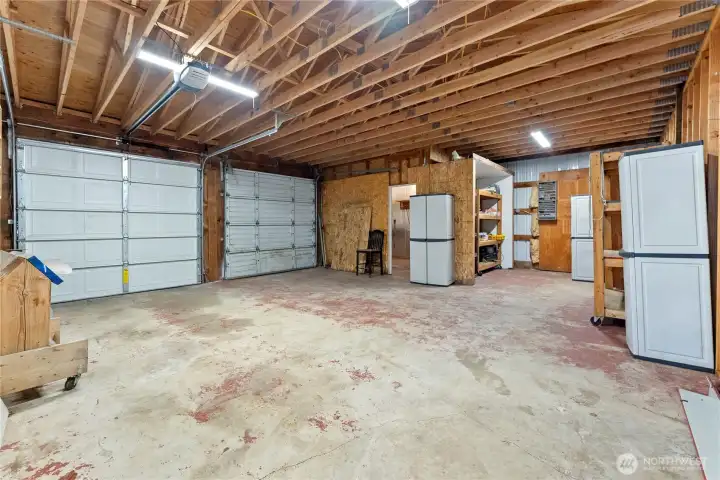 Expansive garage/shop space with double bay doors, insulated storage room, open rafters, and ample storage — perfect for vehicles, projects, or a home workshop.