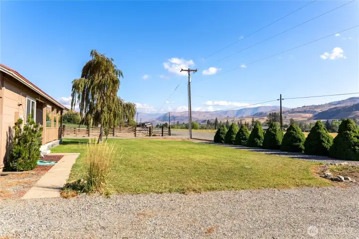 Spacious front lawn with neat landscaping, gravel driveway, and scenic valley views in the background.