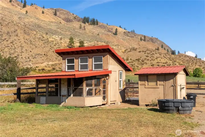 Functional outbuilding and chicken coop with matching roof lines, set within a fenced area — ideal for homesteading or hobby farming.