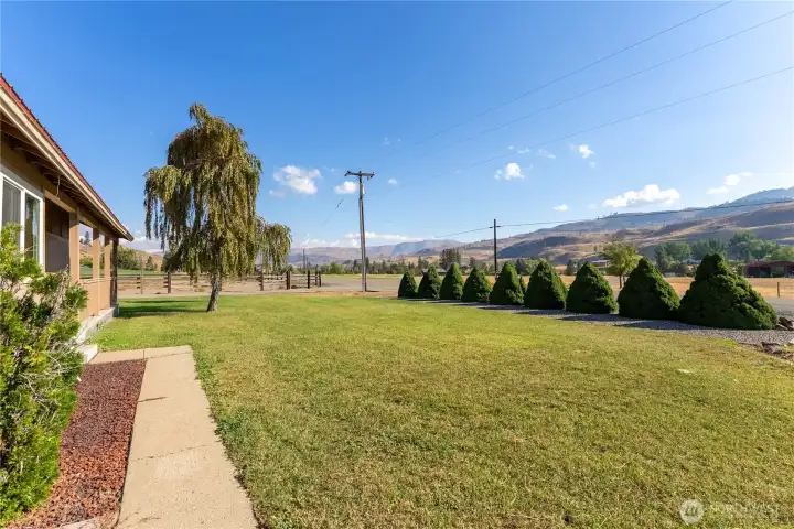 Lush lawn with mature trees and neat landscaping creates a welcoming approach with mountain views beyond.