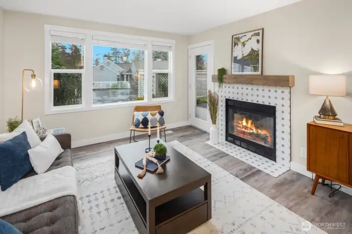 Large living space, with luxury vinyl flooring, wood-burning fireplace with reclaimed wood mantel and Moroccan tile, ample light through a wall of windows.