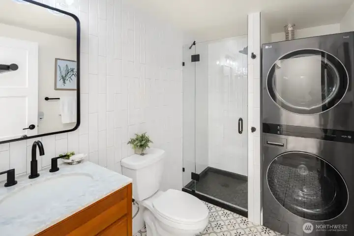 The hall bath showcases more custom tile, marble vanity, shower, and an in-unit modern washer/dryer for added convenience.