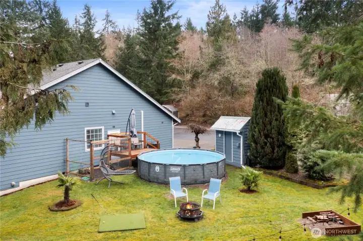 Backyard retreat featuring an above-ground pool, deck, fire pit area, and open lawn space surrounded by mature trees.