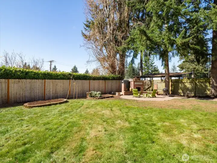 Expansive fully fenced backyard with fire pit and garden beds.