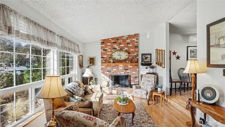 Step inside to a bright living room featuring vaulted ceilings and a warm brick fireplace that creates a welcoming gathering space.