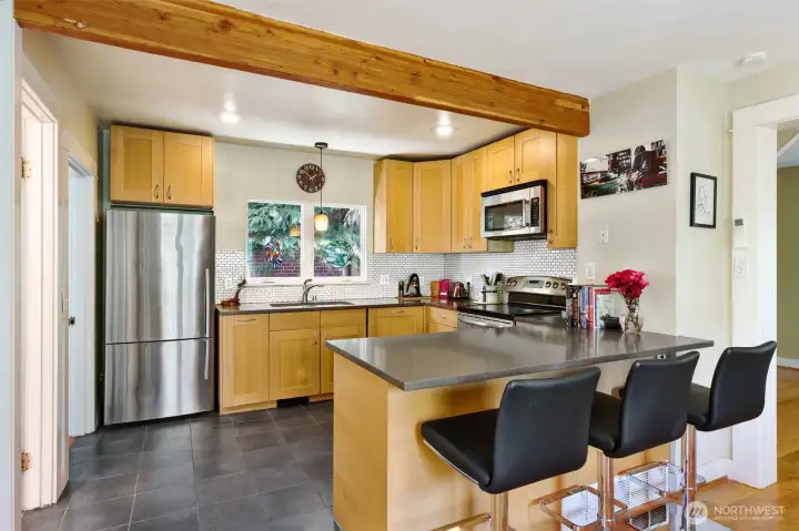 Open updated kitchen with blonde Shaker cabs, quartz countertops, tile floor, and stainless appliances.