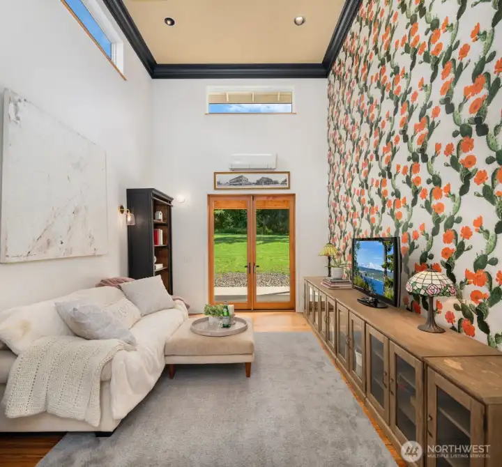 The flex space features soaring 20+ foot walls that flood the interior with natural light, while French doors open to both the main living spaces and the lush orchard beyond.