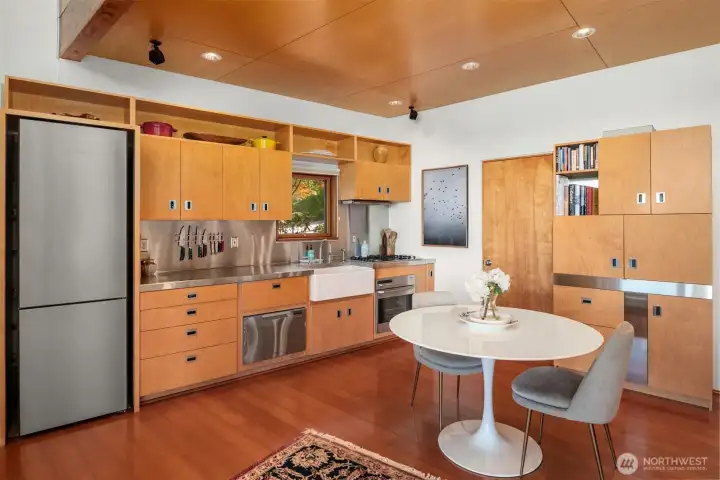 The kitchen showcases high-end new appliances, custom cabinetry, a pull-out mini bar, and striking stainless steel countertops paired with a full-height stainless steel backsplash.