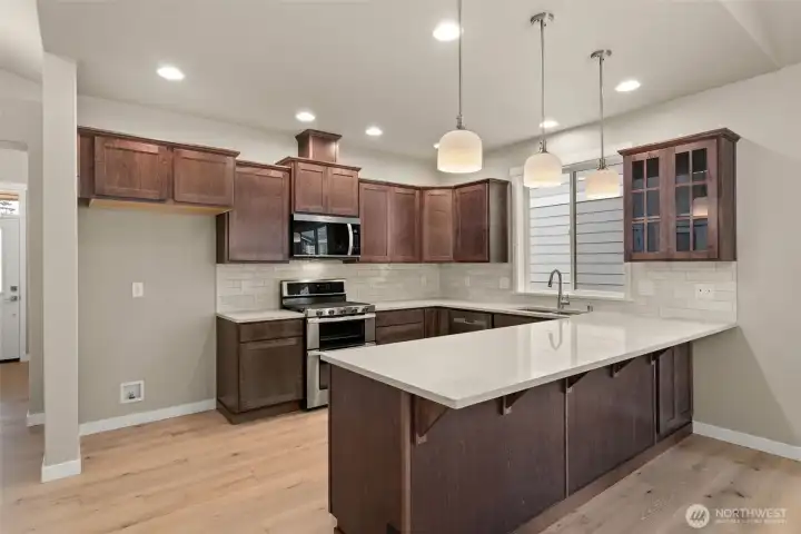 Kitchen features Sable-stained Maple Shaker-style cabinets with quartz countertops and full tile backsplash and extended eating bar.