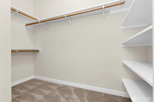 Primary walk-in closet boasts of hanging space and solid wood shelving.