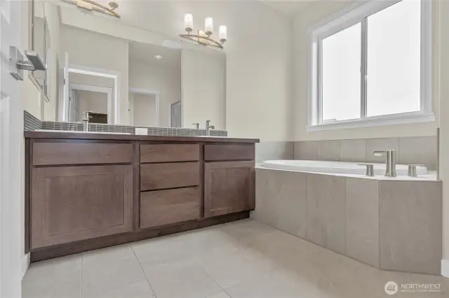 Primary bathroom has a double vanity with undermount dual sinks, tile floor, quartz countertops and a soaking tub with tile surround.