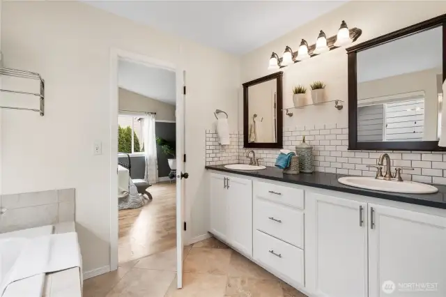 A view of the 5-piece primary bath featuring a soaking tub, dual vanities, travertine floors, and abundant storage.