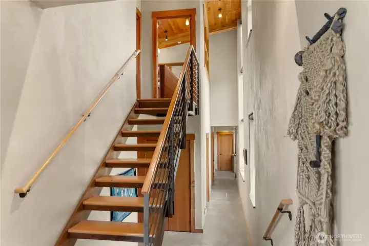 The dramatic hallway of the northwest facing section of the home with access to the primary suite and office upstairs, or downstairs to a second bedroom and bath, laundry and utilities, and a second office at the end of the hall.