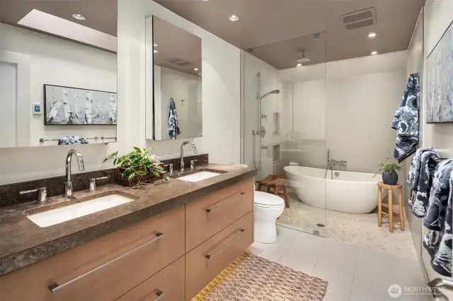 Sumptuous en-suite bath with heated floors, freestanding soaking tub made from composite-granite, rain bar, high-end lighting, in-cabinet electric plugs & extensive storage.