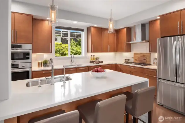 A large breakfast bar seats three with ease. The quartz counters feature a waterfall edge to the right.