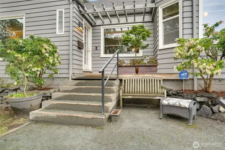 An elevated front porch overlooks thoughtfully landscaped grounds with raised beds and ornamental trees—an inviting spot to start or end your day. Let’s take a look inside.