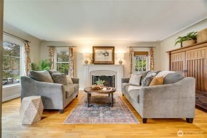 Sunlight pours through large windows, highlighting coved ceilings, crown molding, and a beautifully detailed fireplace with a tile hearth and custom millwork mantle. A nearby door opens to the private side yard—perfect for relaxing evenings.