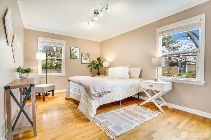 Bright windows on two walls fill this main-floor bedroom with natural light, complemented by hardwood floors and classic crown molding.