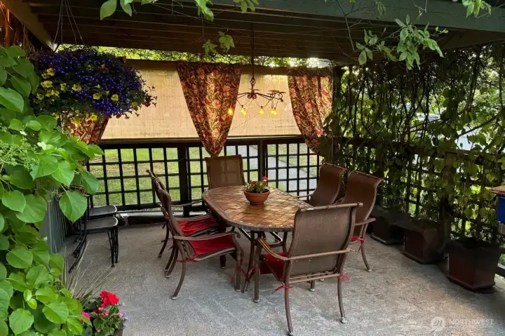 This inviting patio dining area sits beneath a pergola draped in climbing blooms, creating a private, storybook setting—perfect for summer entertaining or relaxed evenings outdoors. Photo provided by owner to illustrate seasonal landscaping as it matures and blooms.