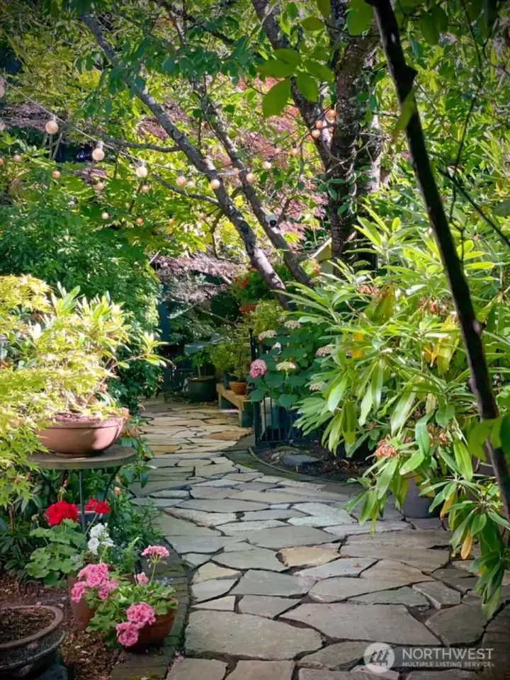 Meander along flagstone paths through lush seasonal landscaping, creating a peaceful backyard escape filled with color and texture. Photo provided by owner to illustrate seasonal landscaping as it matures and blooms.