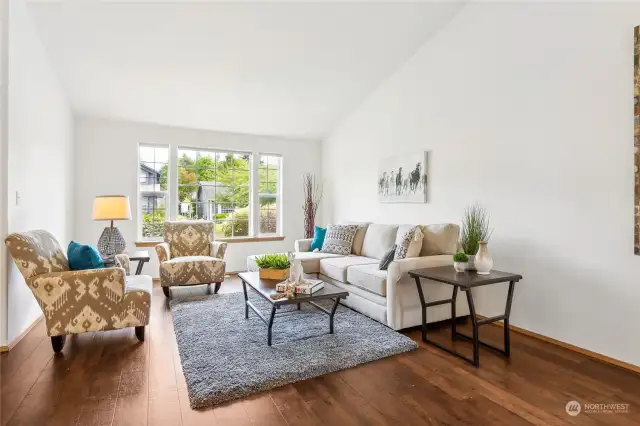 Wide plank wood laminate floors add depth and texture to this vaulted living room with large picture window overseeing the front yard.