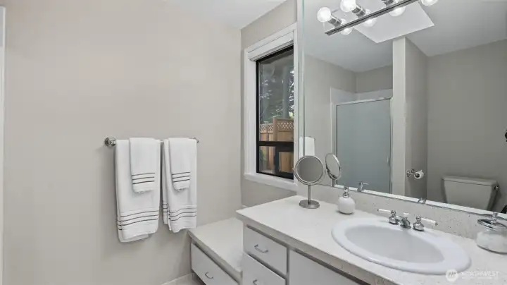 This private ensuite offers spacious counterspace, built-in storage, and a frosted glass shower.