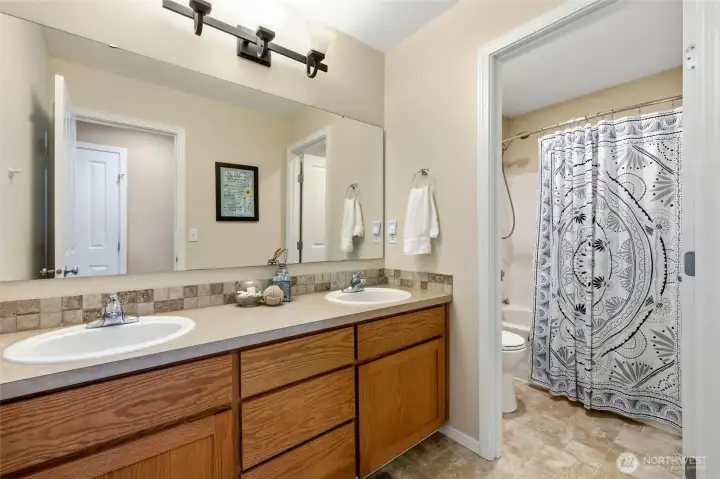 Hall bath with dual vanity and tile backsplash; smart separated design allows for easy sharing. Full tub/shower combo seen ahead.