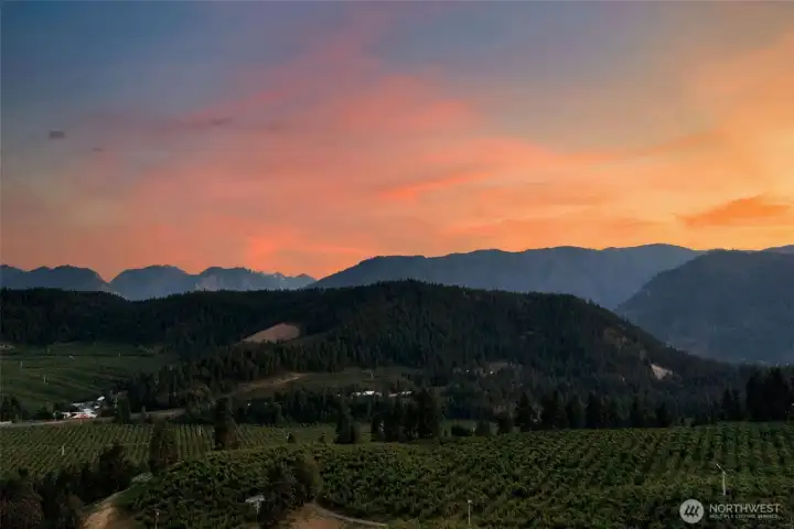 Sweeping views over the valley’s orchards toward the Cascade Mountains and the iconic Enchantment Range, with spectacular sunset skies.