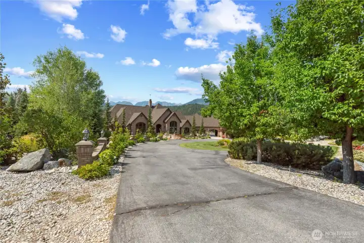 Inviting approach featuring a paved driveway framed by mature trees and natural landscaping, creating a sense of privacy and arrival.