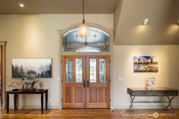 Impressive foyer with soaring ceilings, rich hardwood floors, and beautiful double entry doors topped with a decorative transom window.