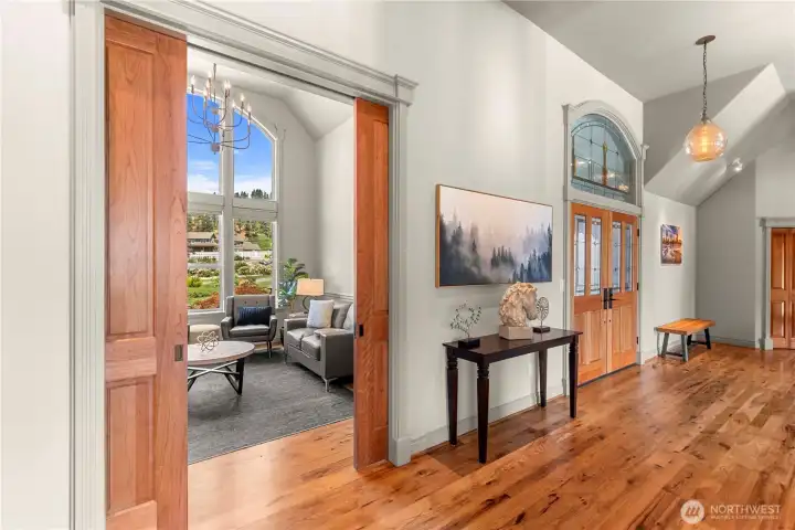Beautifully detailed hallway with hardwood flooring and sliding doors that reveal a bright sitting room framed by a striking arched window.