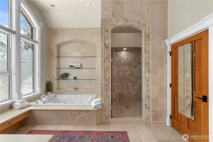 Elegant spa-style primary bath highlighted by a jetted soaking tub, stunning tiled walk-in shower, and custom architectural tilework with built-in niches.