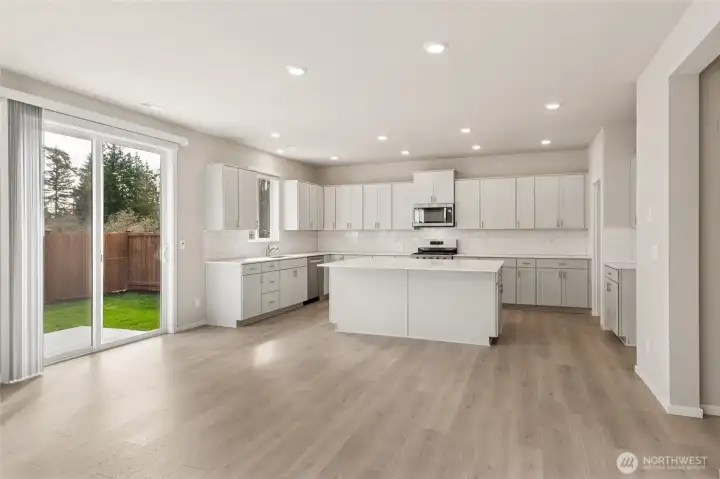 Kitchen and dining area with a large sliding glass door, shaker cabinetry, quartz countertops, center island, stainless steel appliances, and subway tile backsplash. Photos are representative only and may display different color package and/or upgrades.