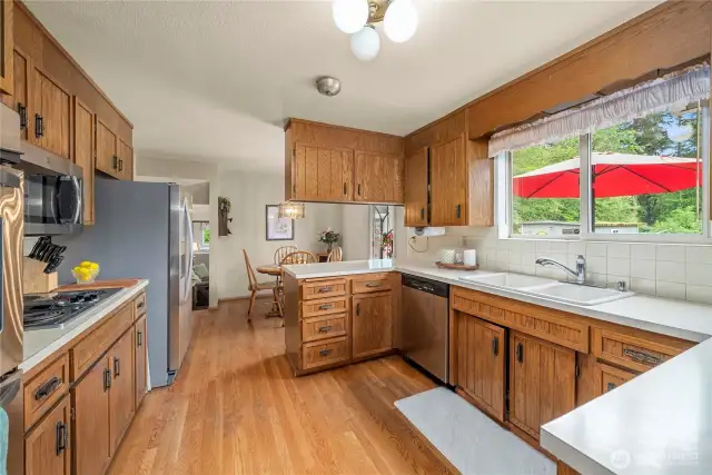 View of kitchen, kitchen eating space, and family room from dining room. Open up that window and pass plates through to the deck guests and back into the kitchen sink. Updated stainless appliances