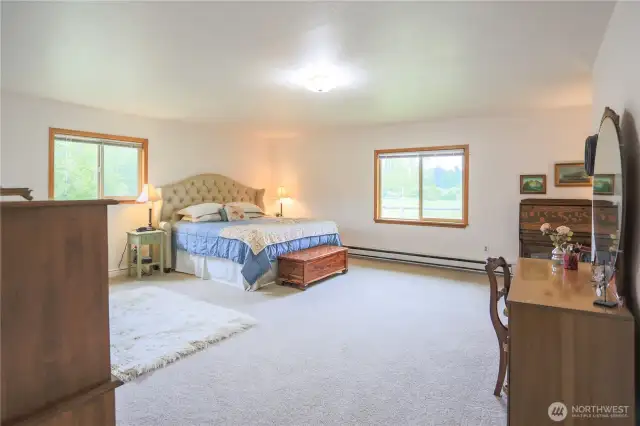 Here’s another peek at the primary bedroom, a space filled with natural light and peaceful views. From these windows, you can look out upon the garden and picturesque acreage, adding to the cozy, restful atmosphere of the bedroom. The view might even inspire you to linger and relax more often.