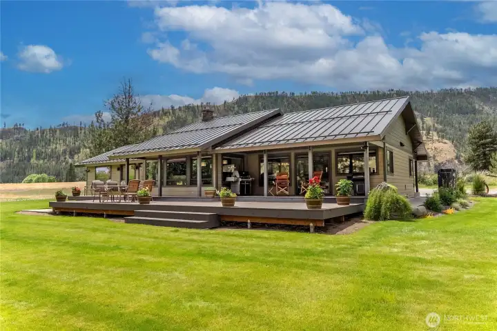 A striking single-level home with a sleek metal roof and expansive deck designed for outdoor living. Surrounded by vibrant green lawn and mountain views, this residence offers the perfect balance of modern elegance and natural tranquility.