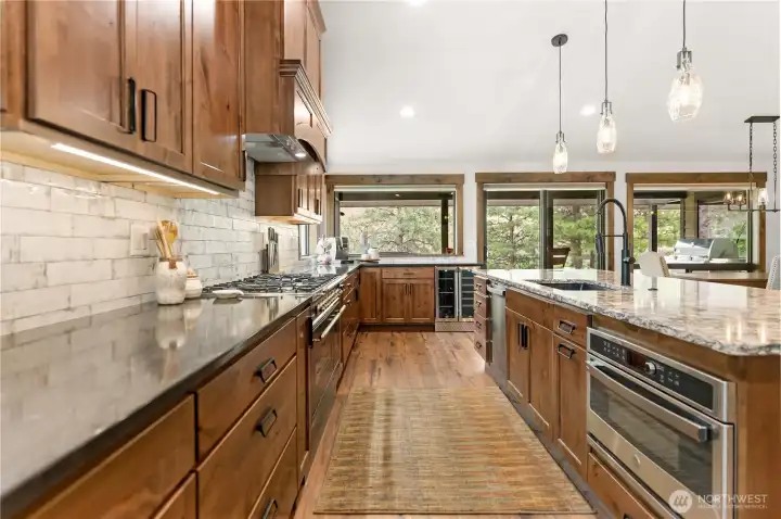 This angle showcases the professional-grade gas range and vent hood, framed by custom tile backsplash and abundant cabinetry for a perfect mix of luxury and practicality.