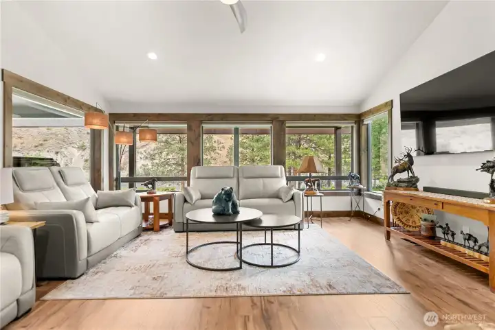 A wall of expansive windows fills this cozy living space with natural light while framing serene views of the surrounding landscape. Neutral tones, elegant wood accents, and contemporary furnishings make this room a stylish yet welcoming retreat.