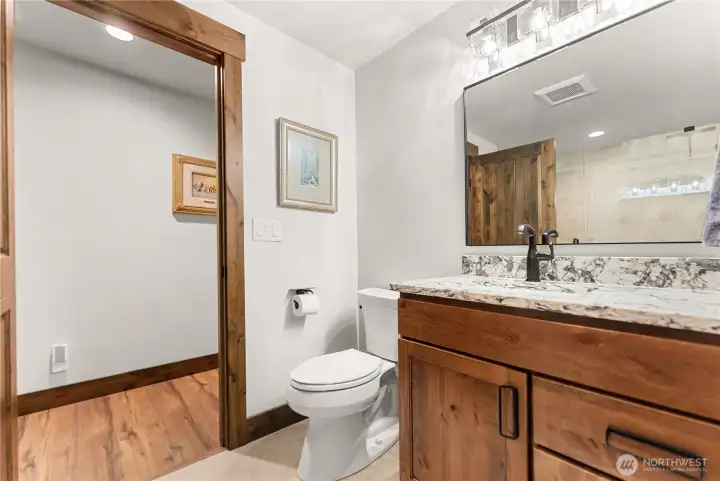 This beautifully designed bathroom features a granite vanity with rich wood cabinetry, oil-rubbed bronze fixtures, and modern lighting. The warm wood trim adds a touch of rustic elegance, creating a spa-like retreat. The walk-in shower impresses with floor-to-ceiling tile, a frameless glass enclosure, and dual showerheads for both style and function. A sleek, contemporary design blends perfectly with timeless finishes.