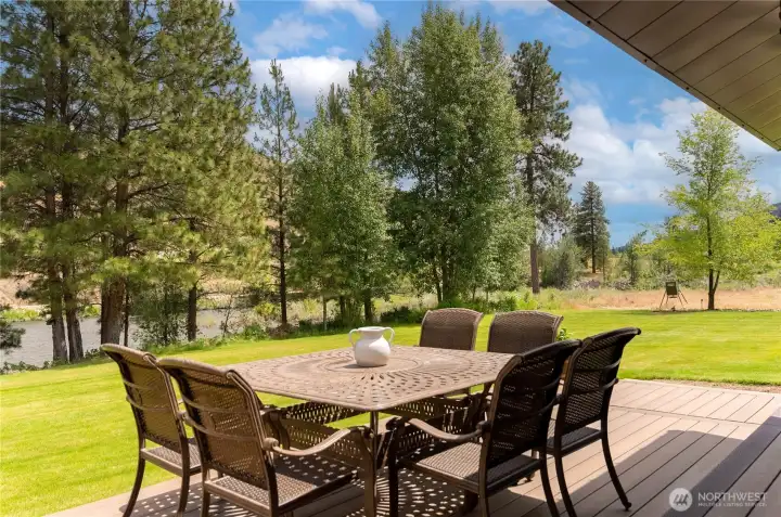 An inviting outdoor dining area with views of the river and surrounding trees provides the perfect setting for entertaining or relaxing. The combination of shade, greenery, and water views makes this space a true extension of the home.