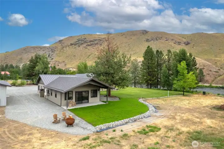 Enjoy serene outdoor living with a lush green lawn, cozy fire pit seating, and stunning mountain views. The covered patio provides the perfect spot to relax or entertain while overlooking the surrounding natural beauty.